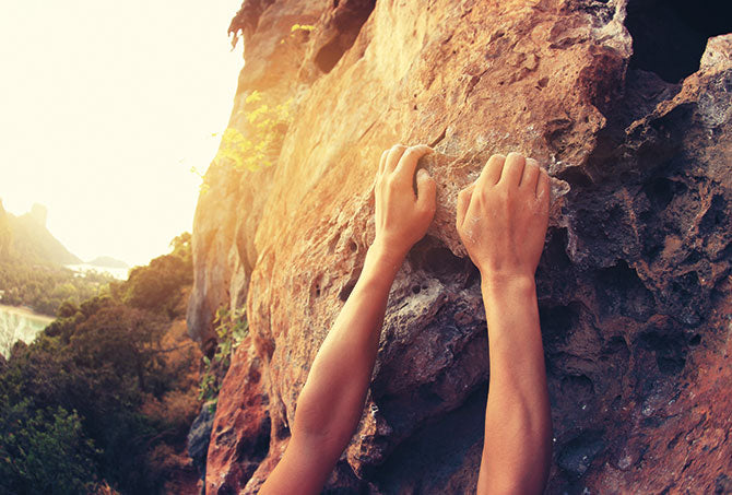 Symbolbild Burnout – Mann hängt mit den Händen am Fels und droht abzustürzen