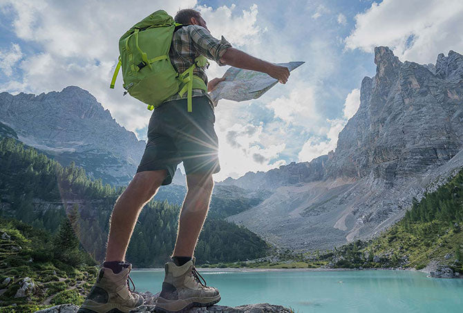 Symbolbild für richtige Zielsetzung: Mann mit Wanderausrüstung in den Bergen hält Wanderkarte in den Händen und sucht das Ziel